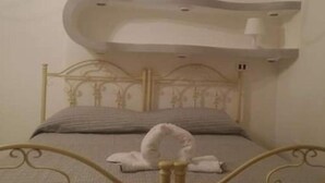 Una cama con estructura metálica y cabecera, una toalla blanca sobre la cama, y un aplique de pared sobre ella.