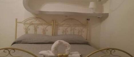 Een bed met een metalen frame en hoofdeinde, een witte handdoek op het bed, en een wandlamp erboven.