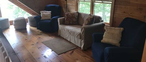 A cozy cabin interior with wooden floors, a sofa, two armchairs, and a lamp.