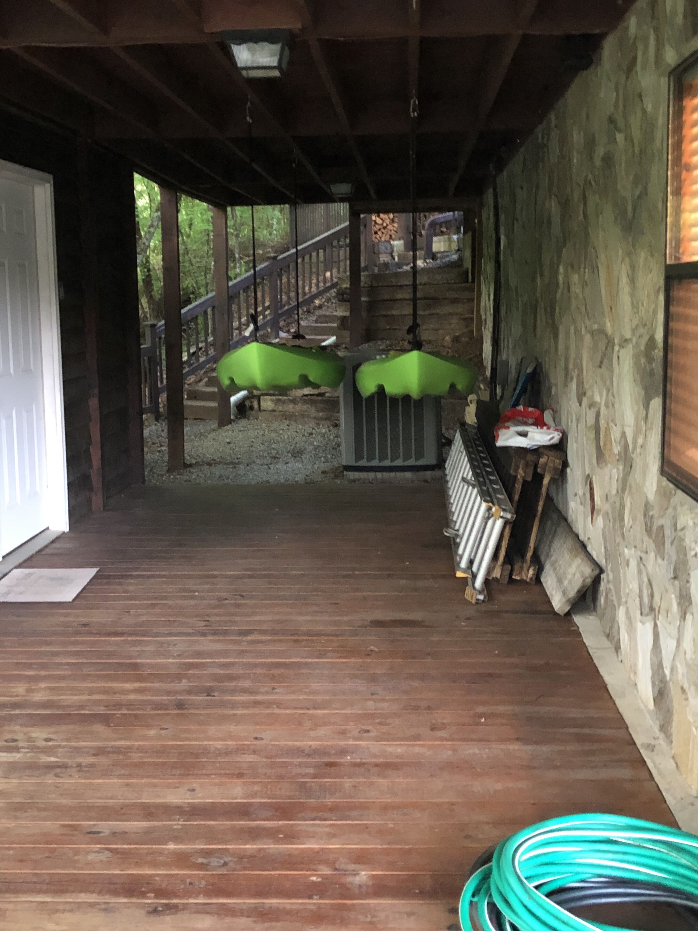 A covered wooden deck with a stone wall, a metal railing, and a green umbrella.