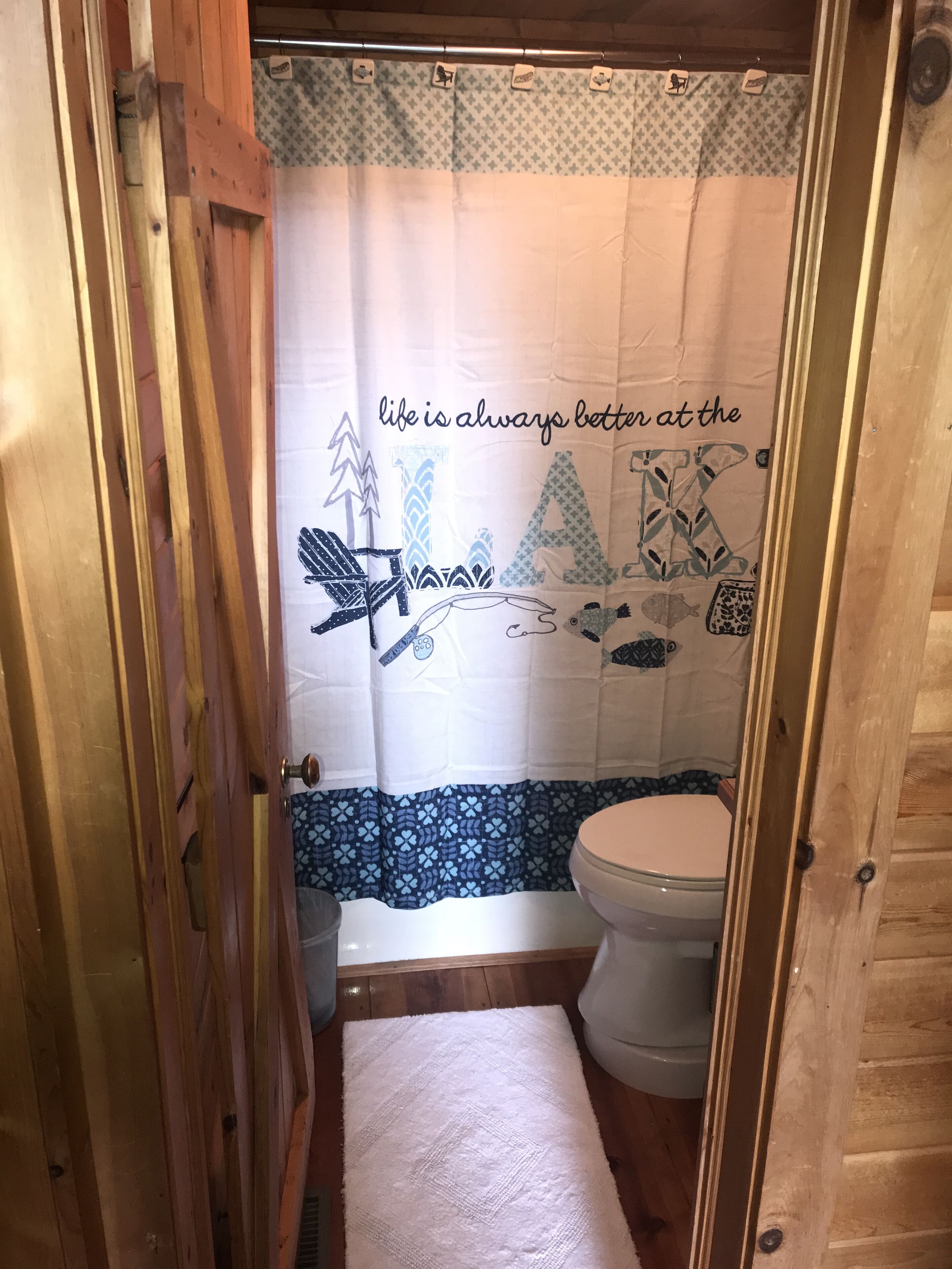 A bathroom with a wooden door, a toilet, and a shower curtain with a nature-themed design.