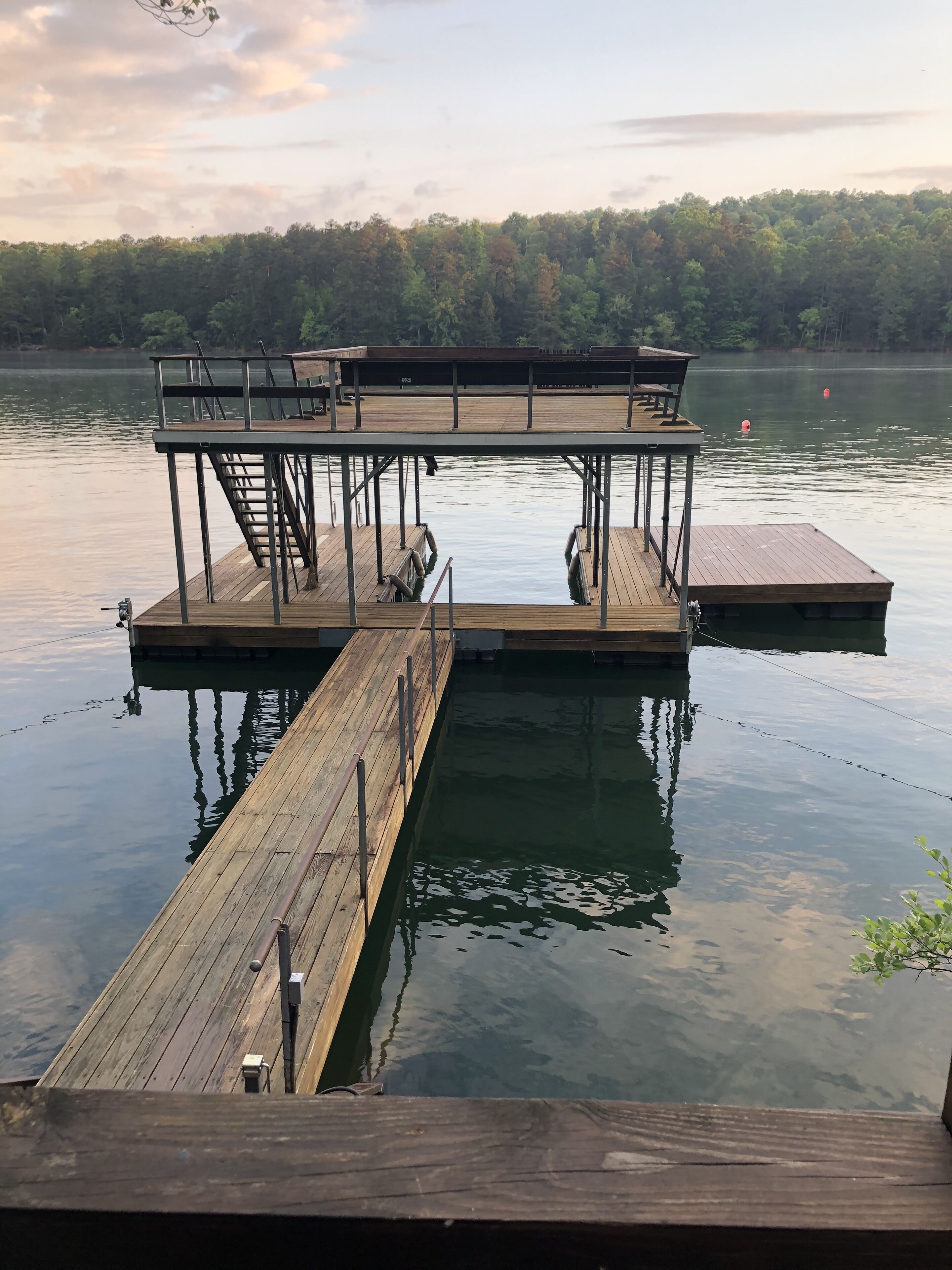 A wooden dock extending into calm water with a platform and stairs.