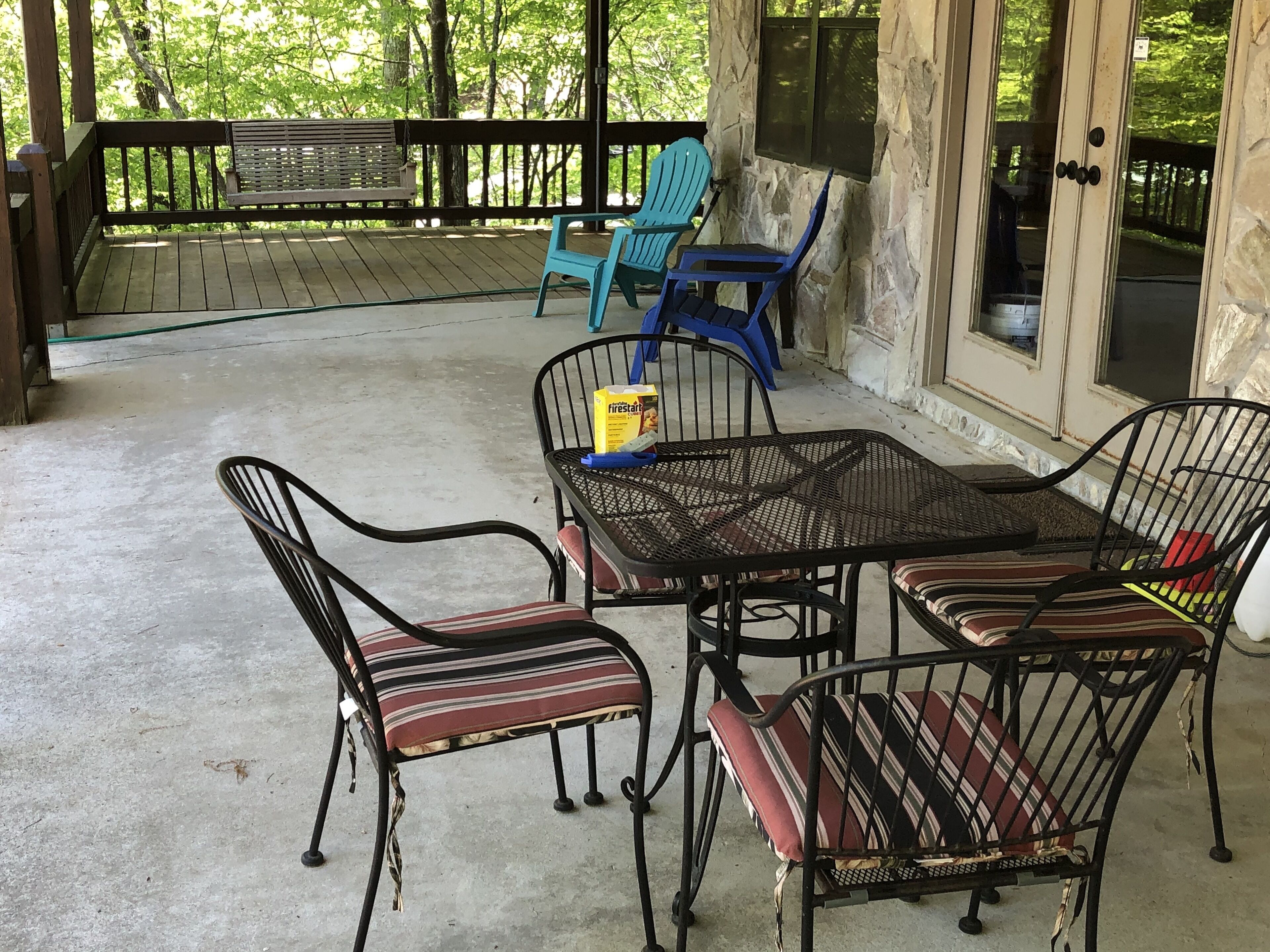 A covered outdoor seating area with a table and chairs, a bench, and a view of trees.