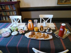 A breakfast table with croissants, juice, honey, jam, and a bottle of ketchup.