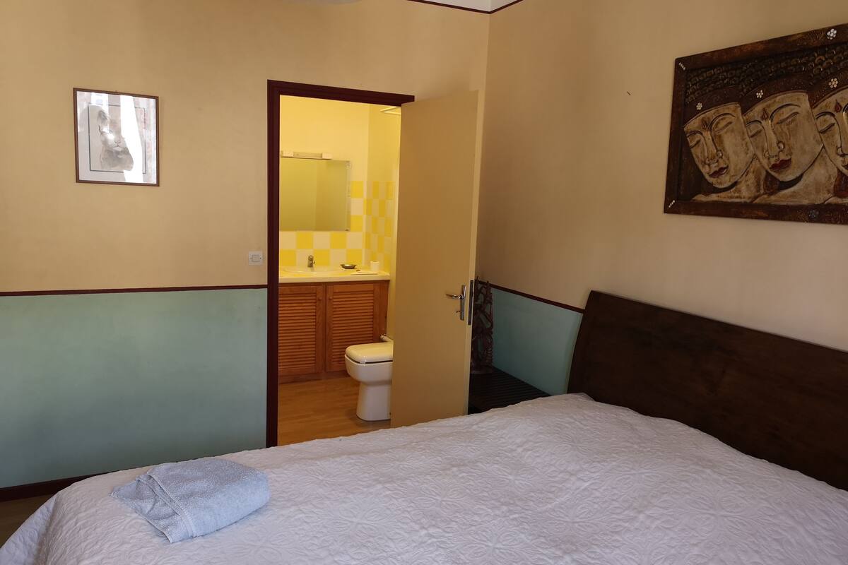 Een slaapkamer met een bed, een badkamer door een open deur zichtbaar en een schilderij aan de muur.