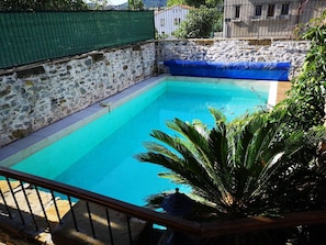A swimming pool with a stone wall and a blue cover, surrounded by greenery.