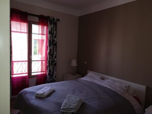 A bedroom with a bed, a nightstand, a lamp, and a window with curtains.