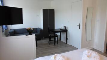 A hotel room with a bed, a desk, a chair, a sofa, a TV, and a wardrobe.