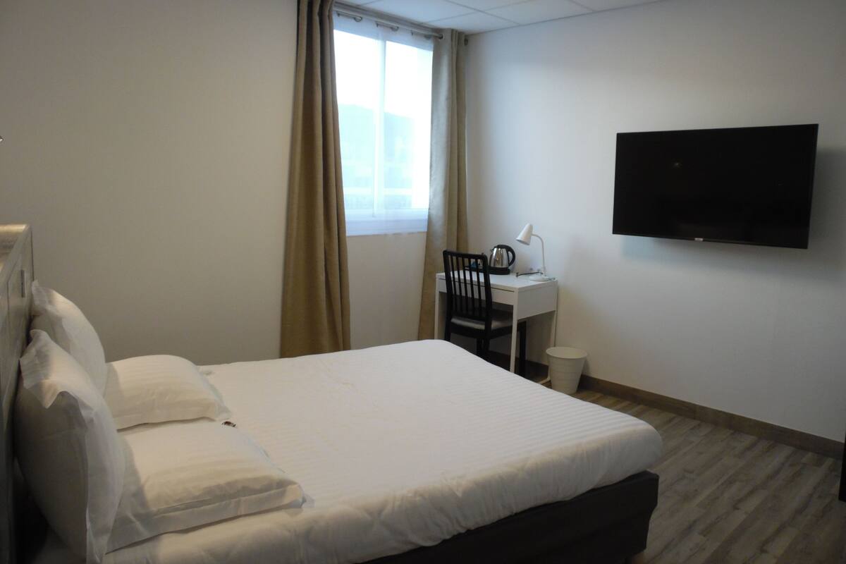 A hotel room with a bed, a desk, a chair, a television, and a window with curtains.