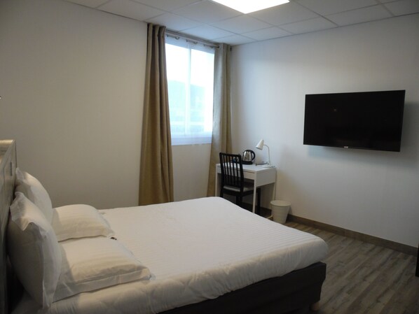 Ein Hotelzimmer mit Bett, Schreibtisch, Stuhl, Fernseher und einem Fenster mit Vorhängen.