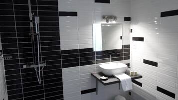 A modern bathroom with black and white tiles, a white sink, a mirror, and a shower.