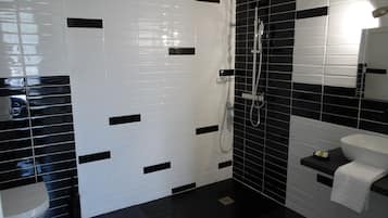 Une salle de bain avec des toilettes blanches, une douche carrelée en noir et blanc et un lavabo avec un miroir.