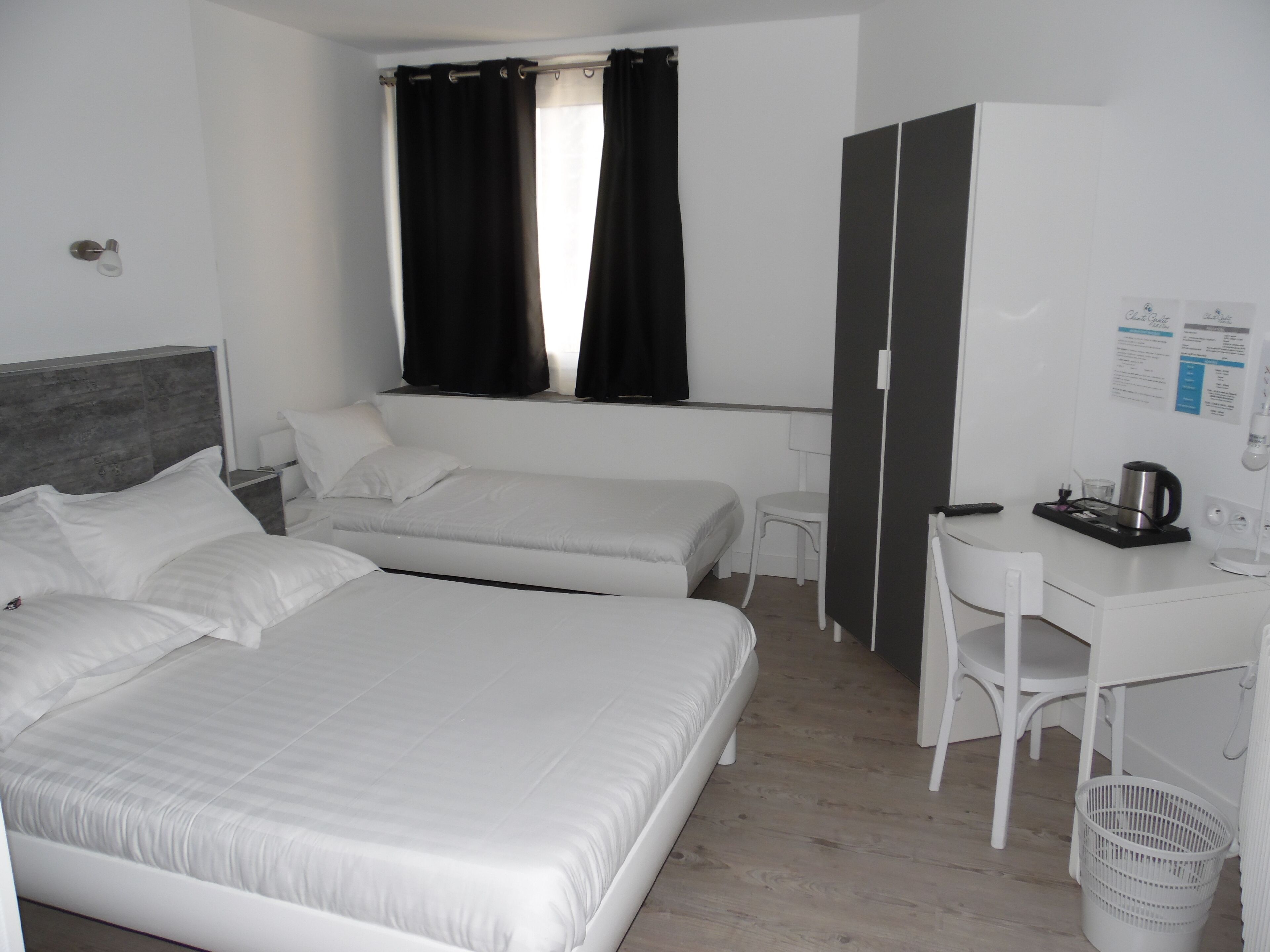 Ein Hotelzimmer mit zwei Einzelbetten, einem Schreibtisch, einem Stuhl, einem kleinen Tisch mit Wasserkocher und einer Mülleimer.