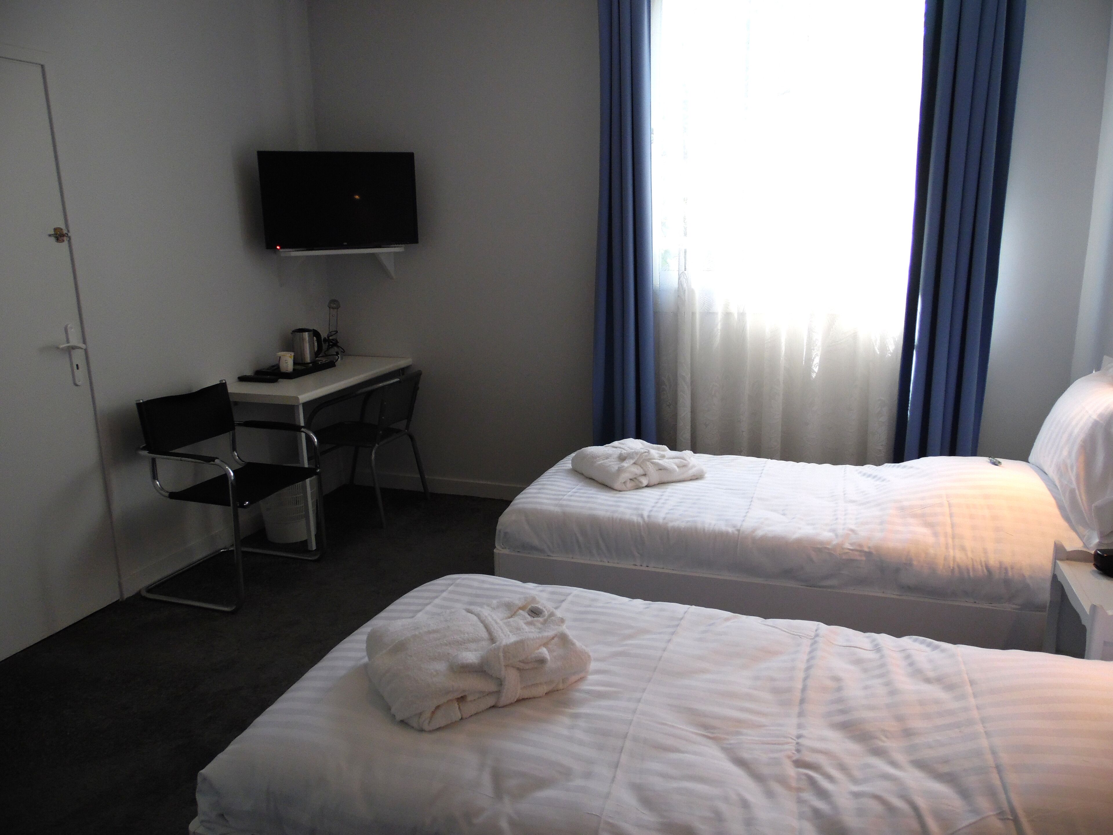 A hotel room with two beds, a desk, a chair, a TV, and a window with curtains.