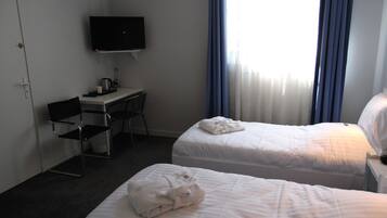 A hotel room with two beds, a desk, a chair, a TV, and a window with curtains.