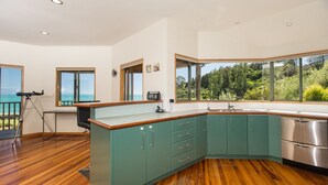 A modern kitchen with teal cabinets, a wooden countertop, and a view of the ocean.