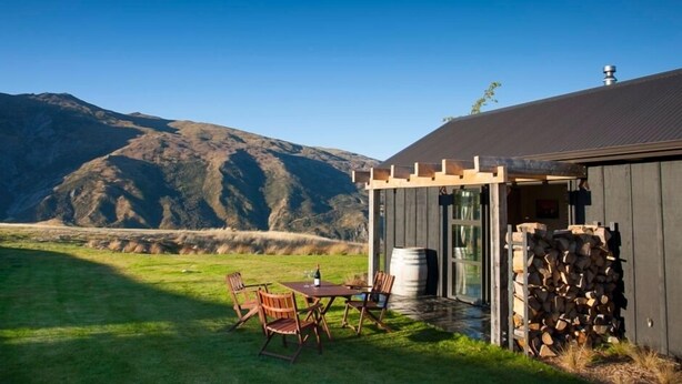 A rustic outdoor seating area with a table and chairs, a wooden pergola, and a stack of firewood. - Up in the mountains!!! Luxury self contained unit. (Arrowtown)