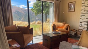 A modern living room with a sofa, armchair, and a wooden coffee table. A large window offers a view of a mountainous landscape. - Up in the mountains!!! Luxury self contained unit. (Arrowtown)