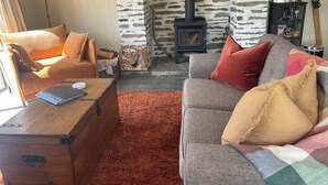 A cozy living room with a stone wall, a wooden stove, a sofa, and a suitcase. - Up in the mountains!!! Luxury self contained unit. (Arrowtown)