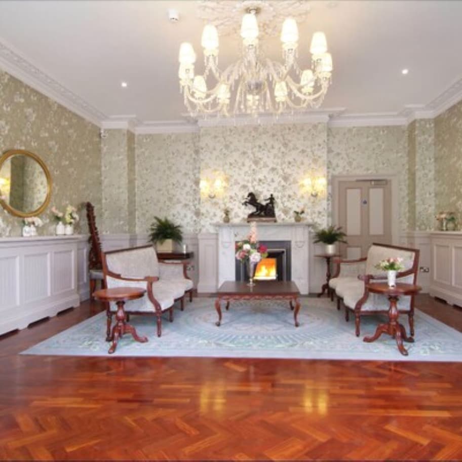 A formal room with a fireplace, two armchairs, a coffee table, and a chandelier.