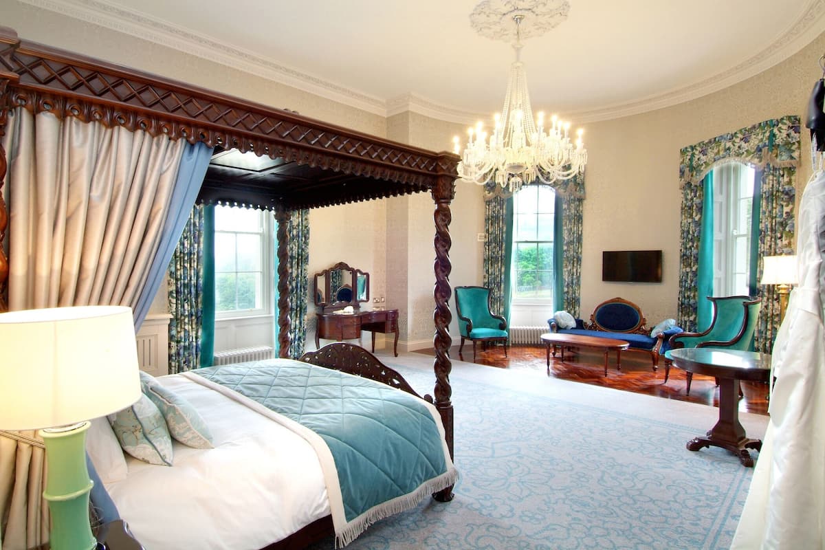 A spacious bedroom with a four-poster bed, a chandelier, and a large window with curtains.
