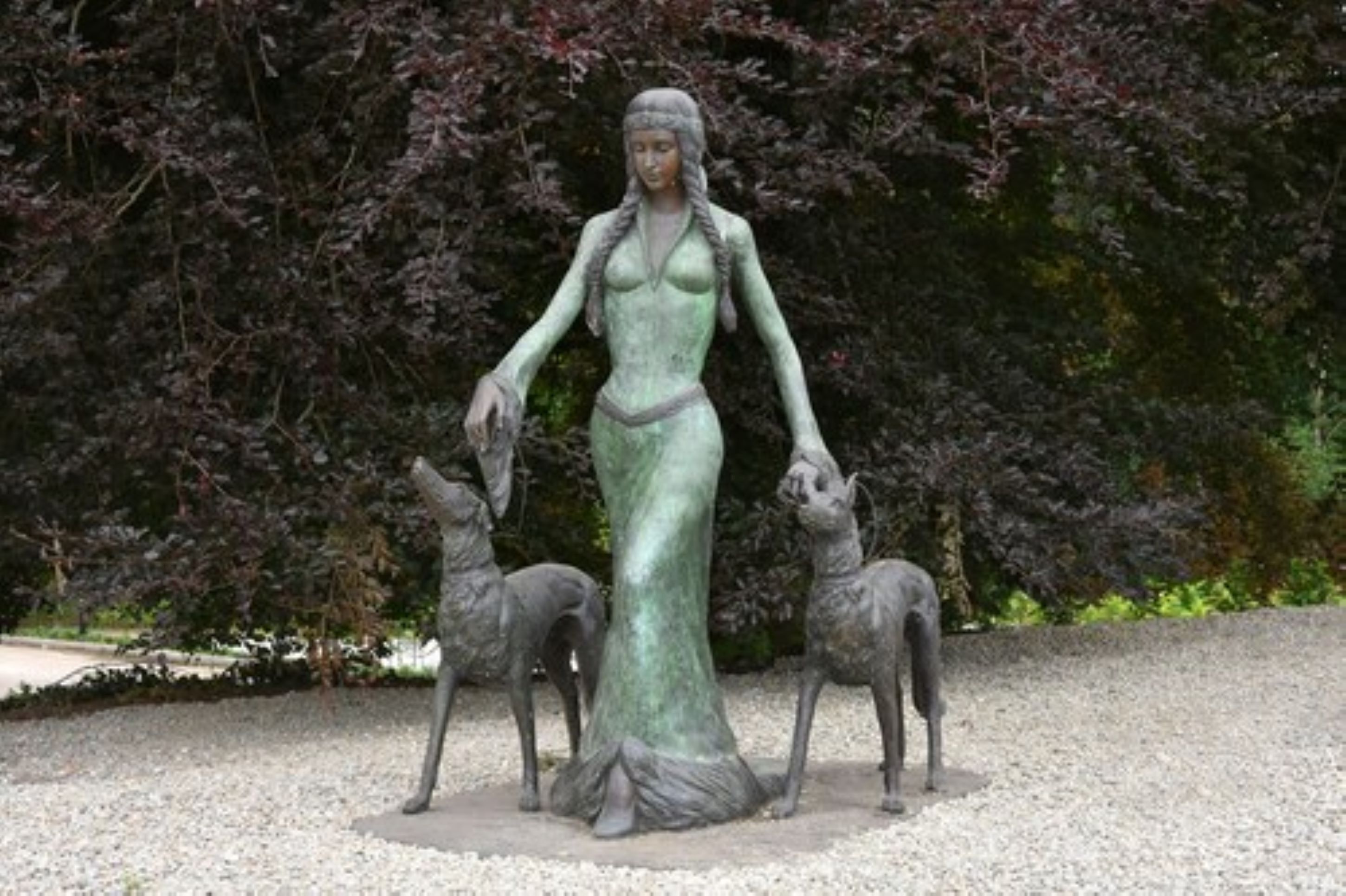 A statue of a woman with two deer in a garden setting.