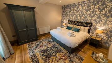 A bedroom with a large bed, dark wardrobe, floral wallpaper, and a patterned rug.