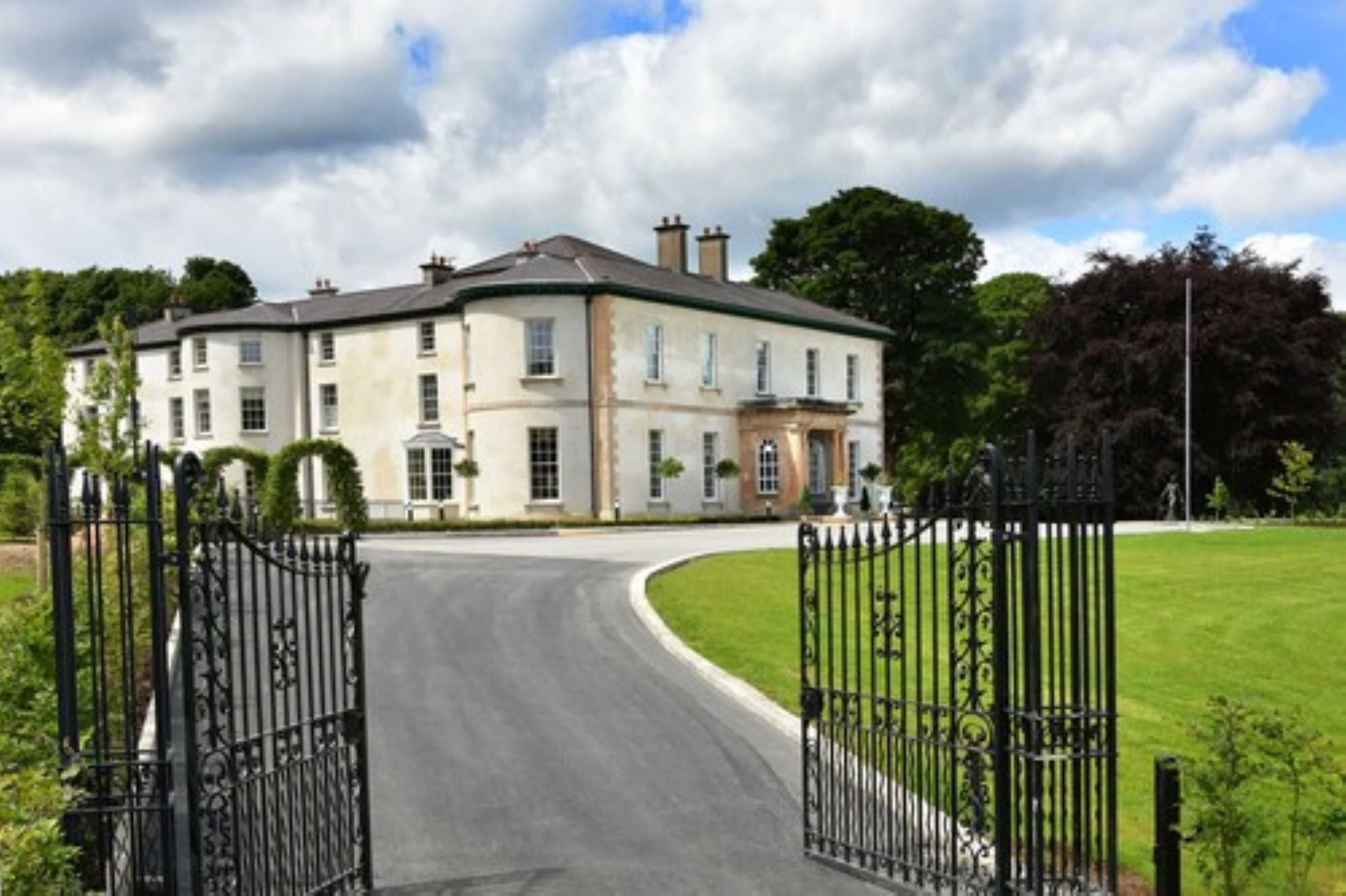 A large, two-story building with a curved driveway and black wrought iron gates.