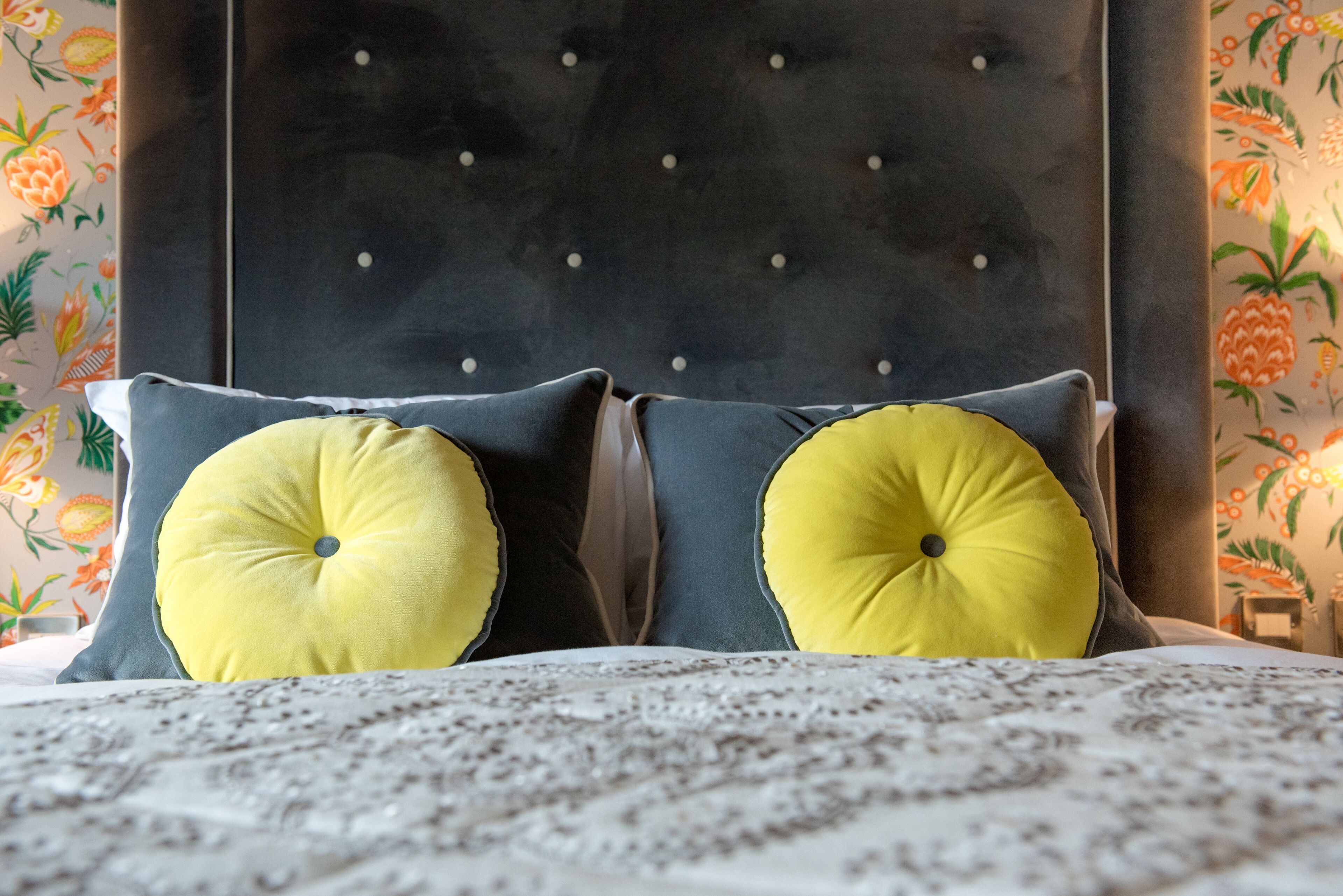 Un letto con testiera imbottita, due cuscini con motivo giallo e copripiumino decorato.