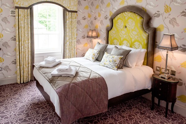 A neatly made bed with a patterned bedspread and pillows, a bedside lamp, and a window with curtains. - Rockhill House (Letterkenny)