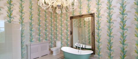 A bathroom with a freestanding bathtub, a large mirror, and a chandelier.