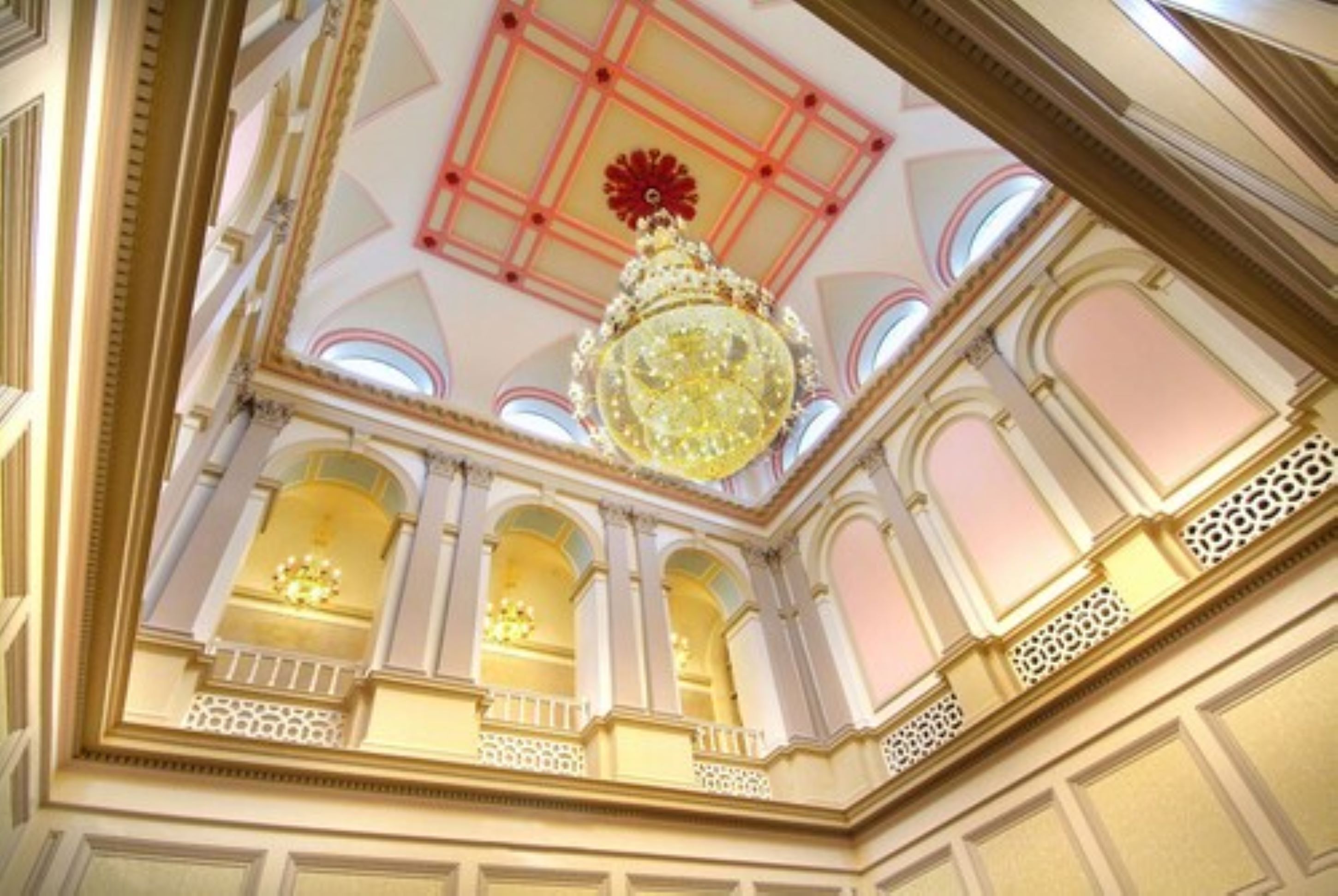 Un interior imponente con una gran lámpara de araña, ventanas arqueadas y detalles ornamentales en el techo.