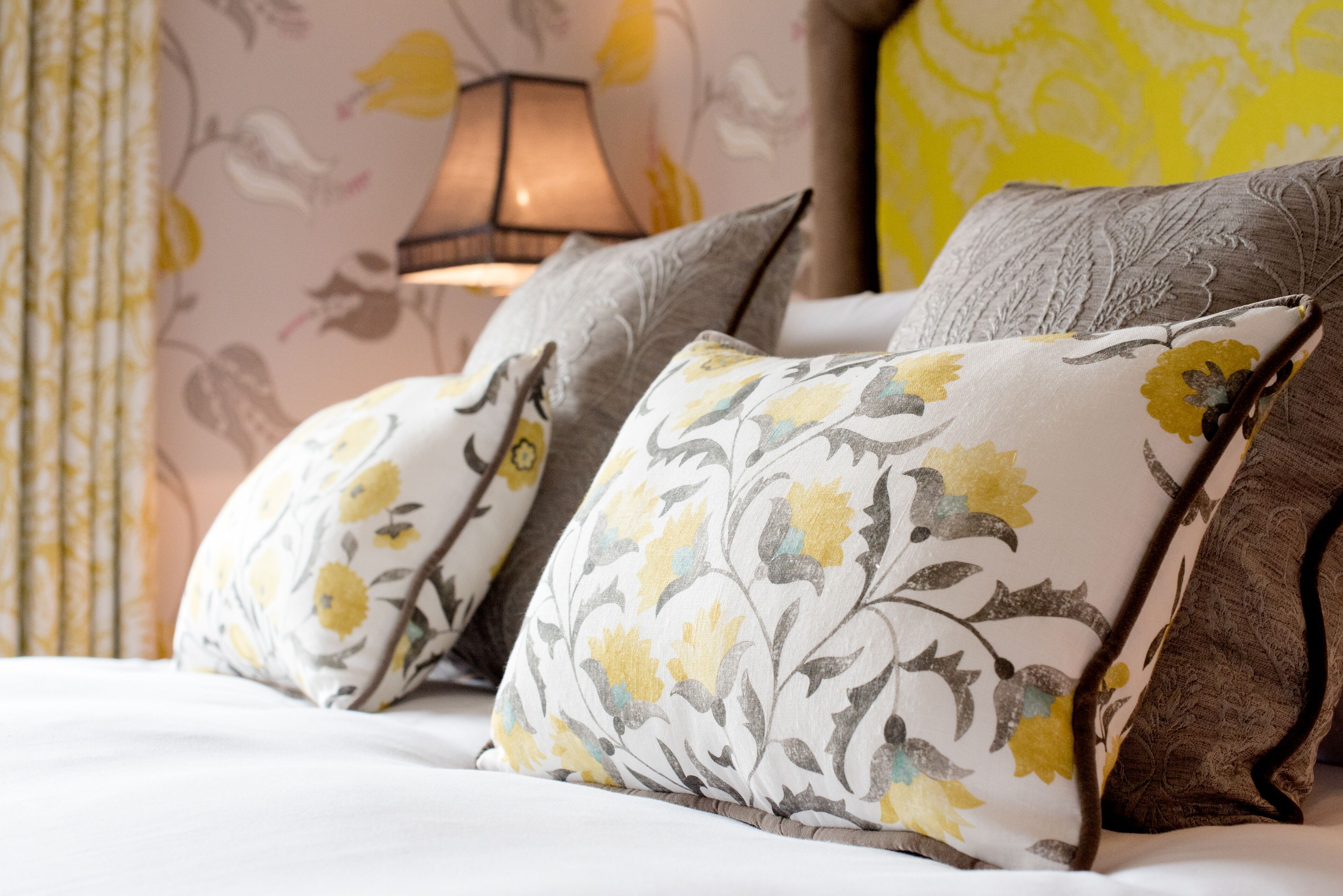 Una cama con almohadas de estampado floral y una lámpara al fondo.