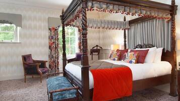 Una cama con dosel y cuatro columnas, con una manta roja, una silla de madera y una alfombra estampada.