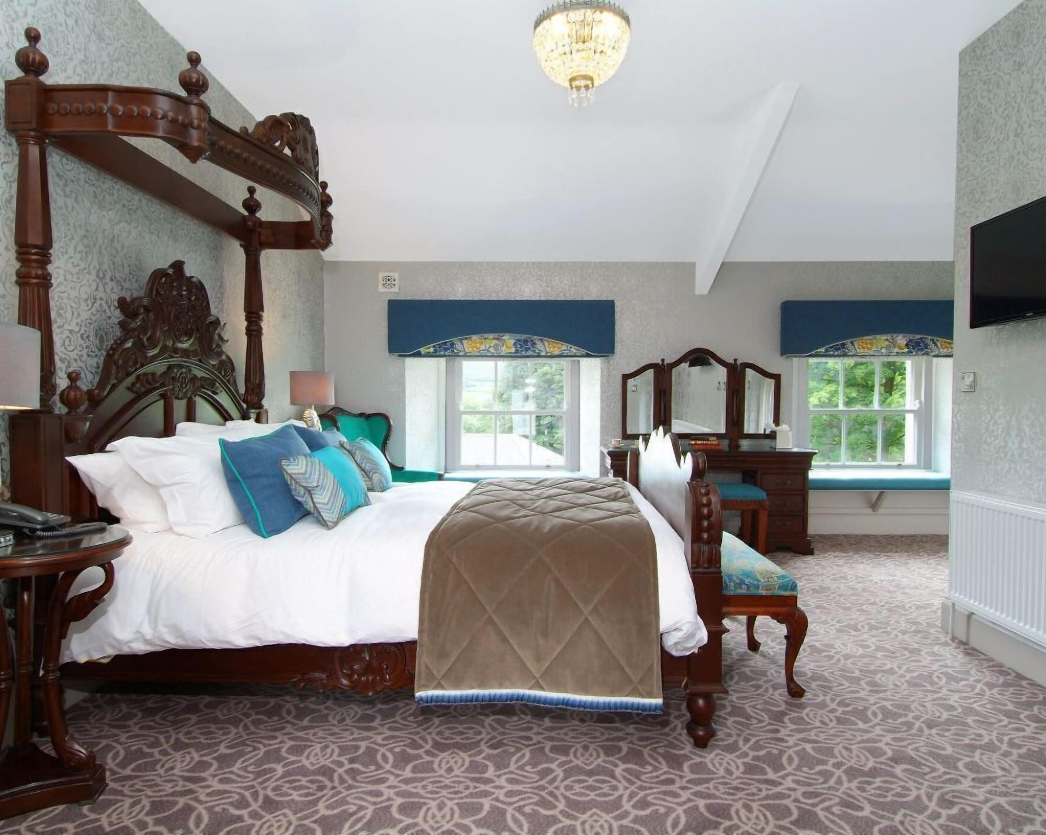 A spacious bedroom with a large bed, a dresser, a vanity, and a television.