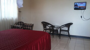 Una habitación de hotel con una cama, dos sillas, una mesita y un televisor montado en la pared.