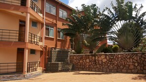 Un edificio de varios pisos con balcones, un muro de piedra y plantas tropicales.