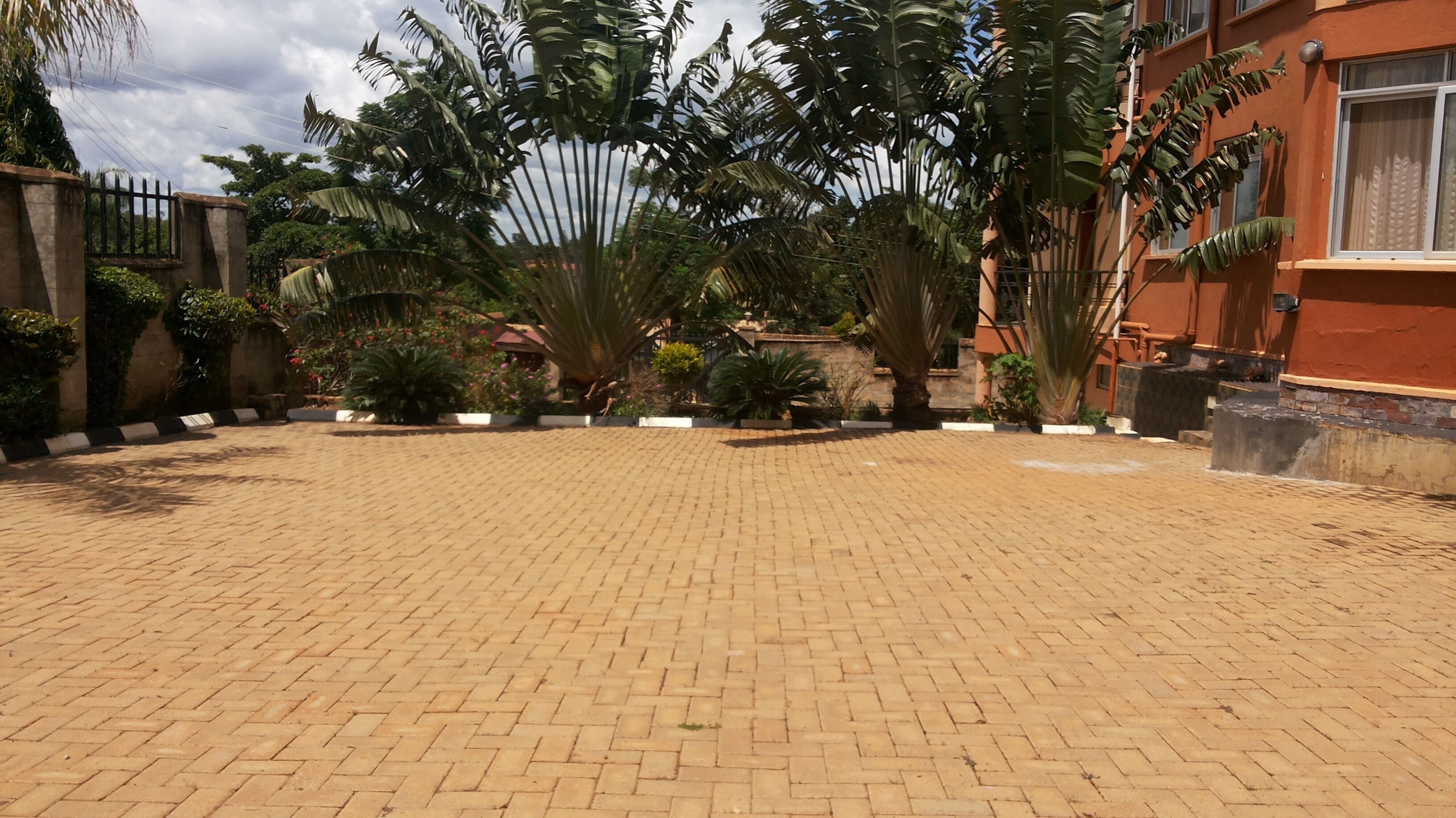 Un cortile pavimentato con un motivo a mattoni, circondato da rigogliosa vegetazione tropicale e un edificio con facciata rossa.