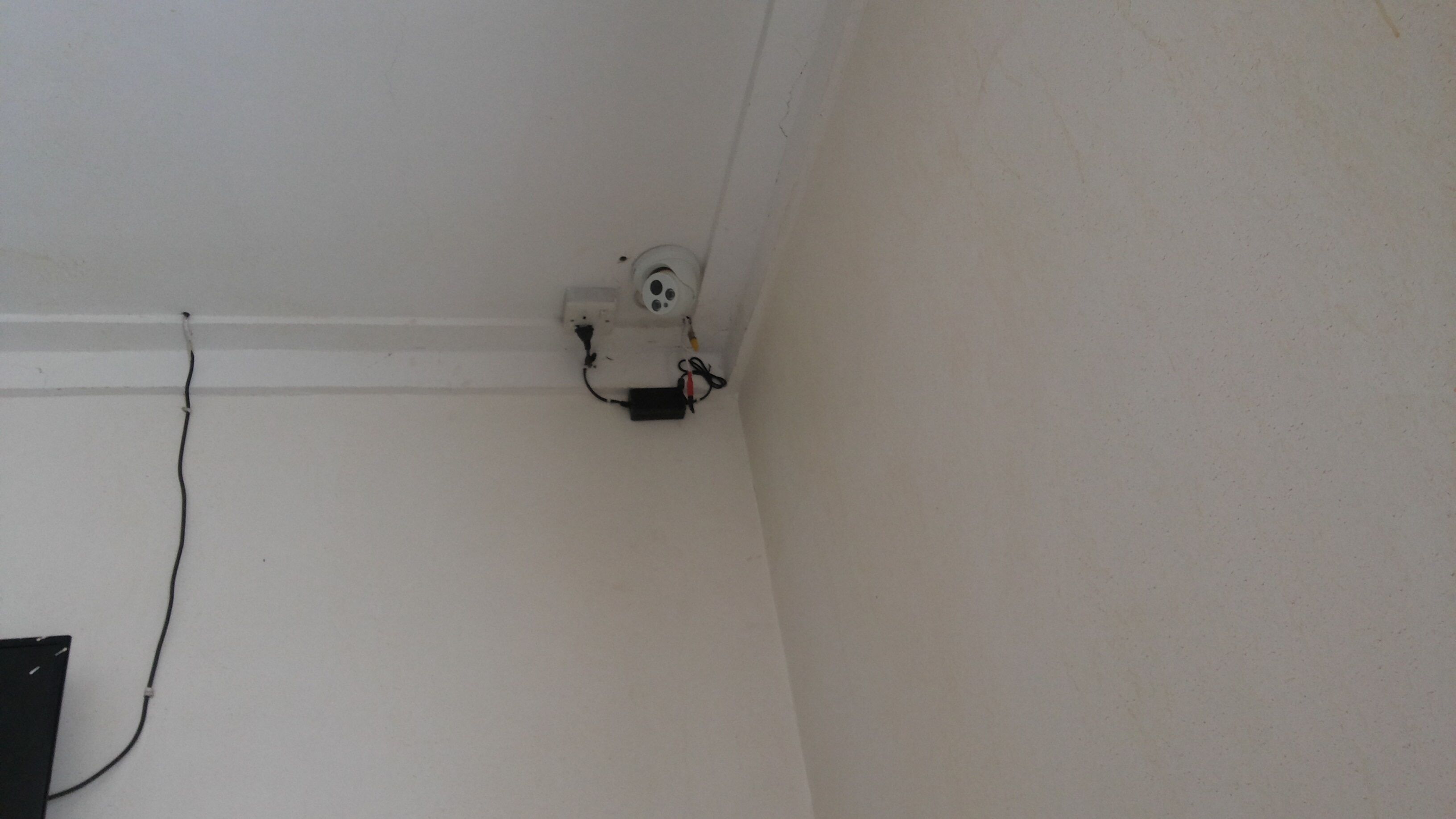 En del av ett rum med en vit vägg, ett synligt eluttag och en svart kabel som löper längs väggen.