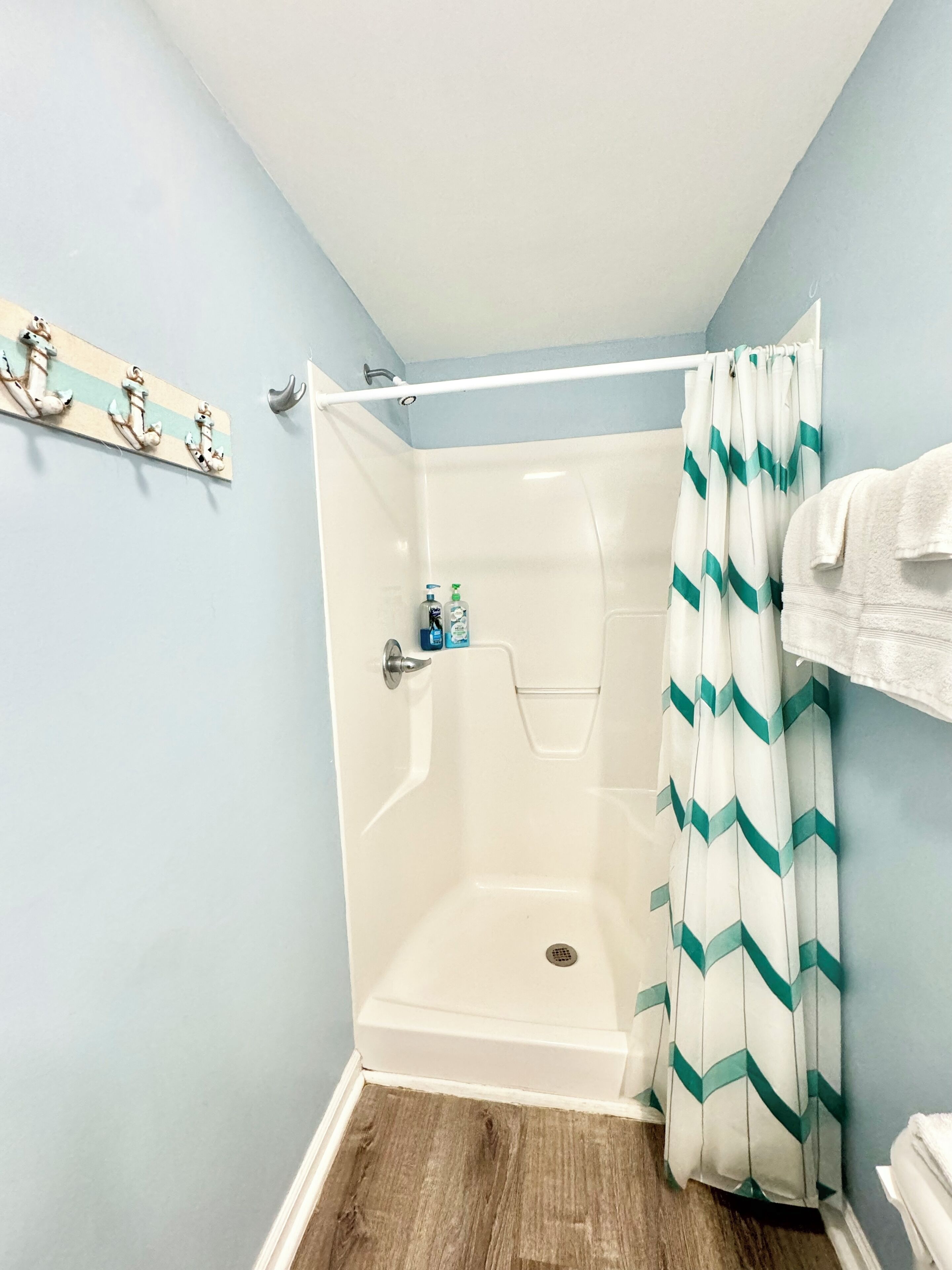 A small, enclosed shower area with a white shower curtain and a wooden coat rack with decorative items.