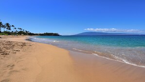 Une plage avec une eau d’un bleu limpide, un rivage sablonneux et une montagne en arrière-plan.