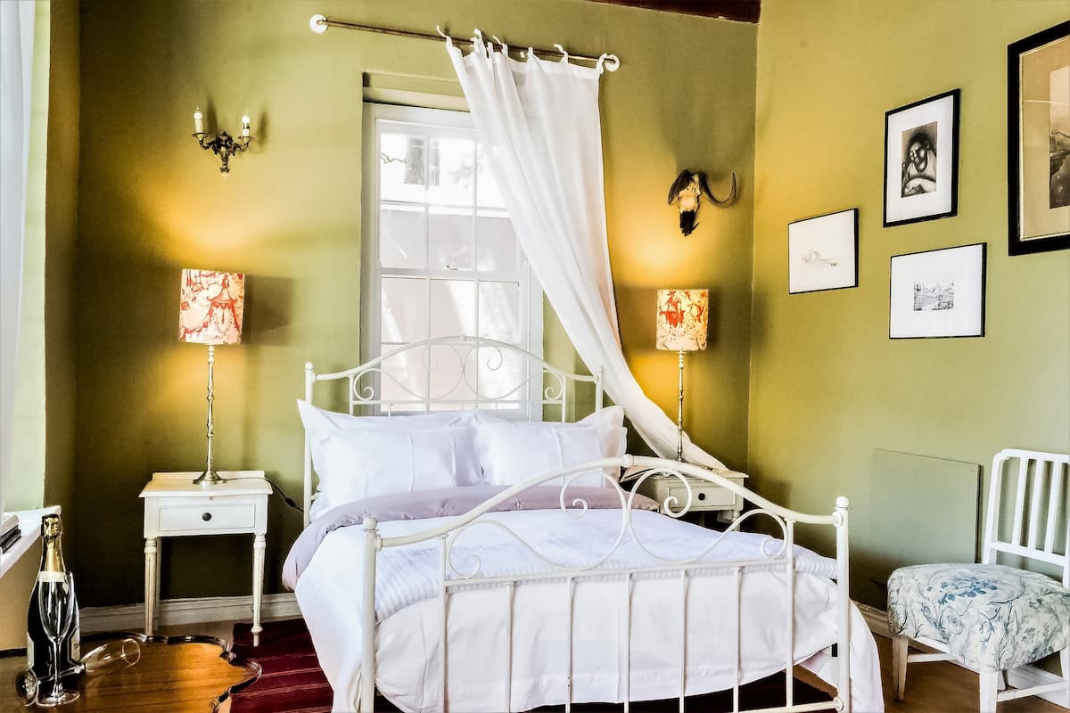 Un dormitorio ordenado con cama, mesitas de noche, una silla y cuadros en la pared.