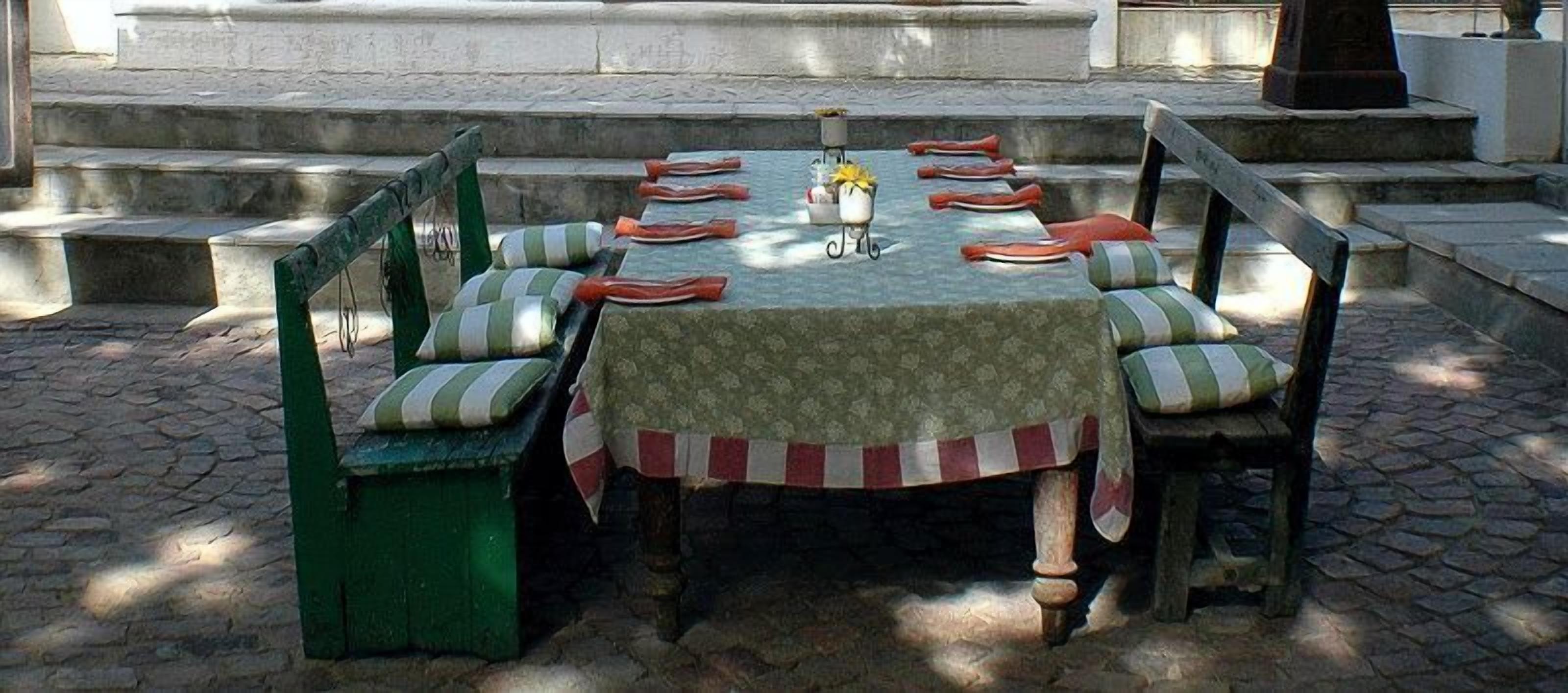 A round table with a patterned tablecloth, surrounded by wooden chairs with striped cushions.