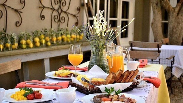 A breakfast table set with plates of food, drinks, and a vase of flowers. -  Old Oak Manor (Riebeek Kasteel)