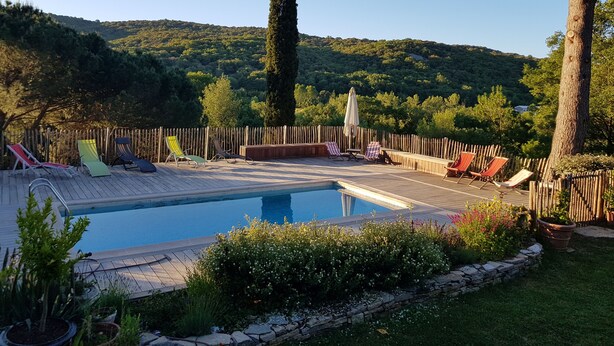 A pool with lounge chairs and a wooden deck, surrounded by greenery and a wooden fence. - Mas des Ballats (Saint-Bauzille-de-Putois)