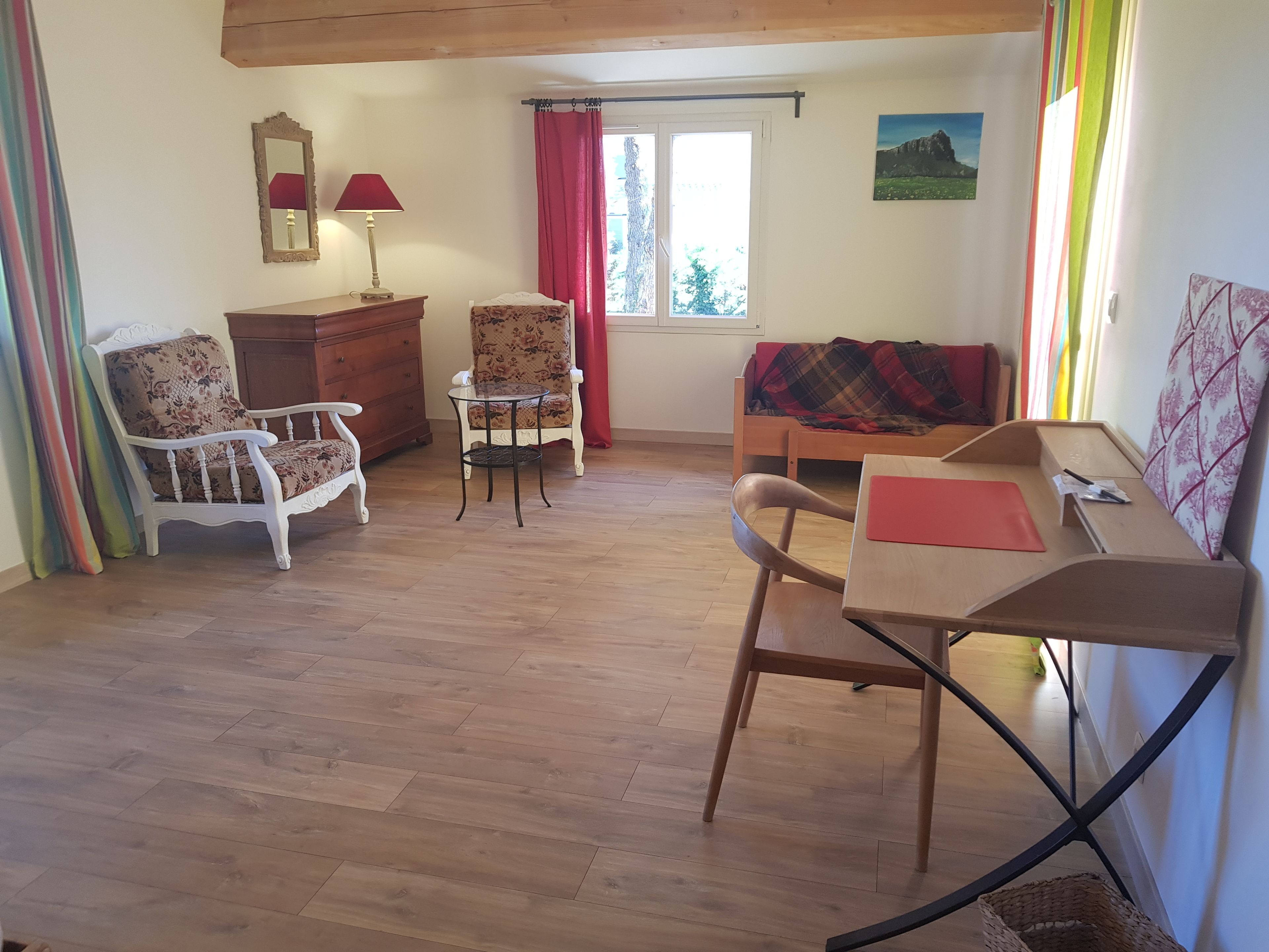Een knus ingerichte kamer met houten vloer, een houten tafel, twee stoelen, een bank, een dressoir en een raam met gordijnen.