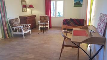 Een knus ingerichte kamer met houten vloer, een houten tafel, twee stoelen, een bank, een dressoir en een raam met gordijnen.
