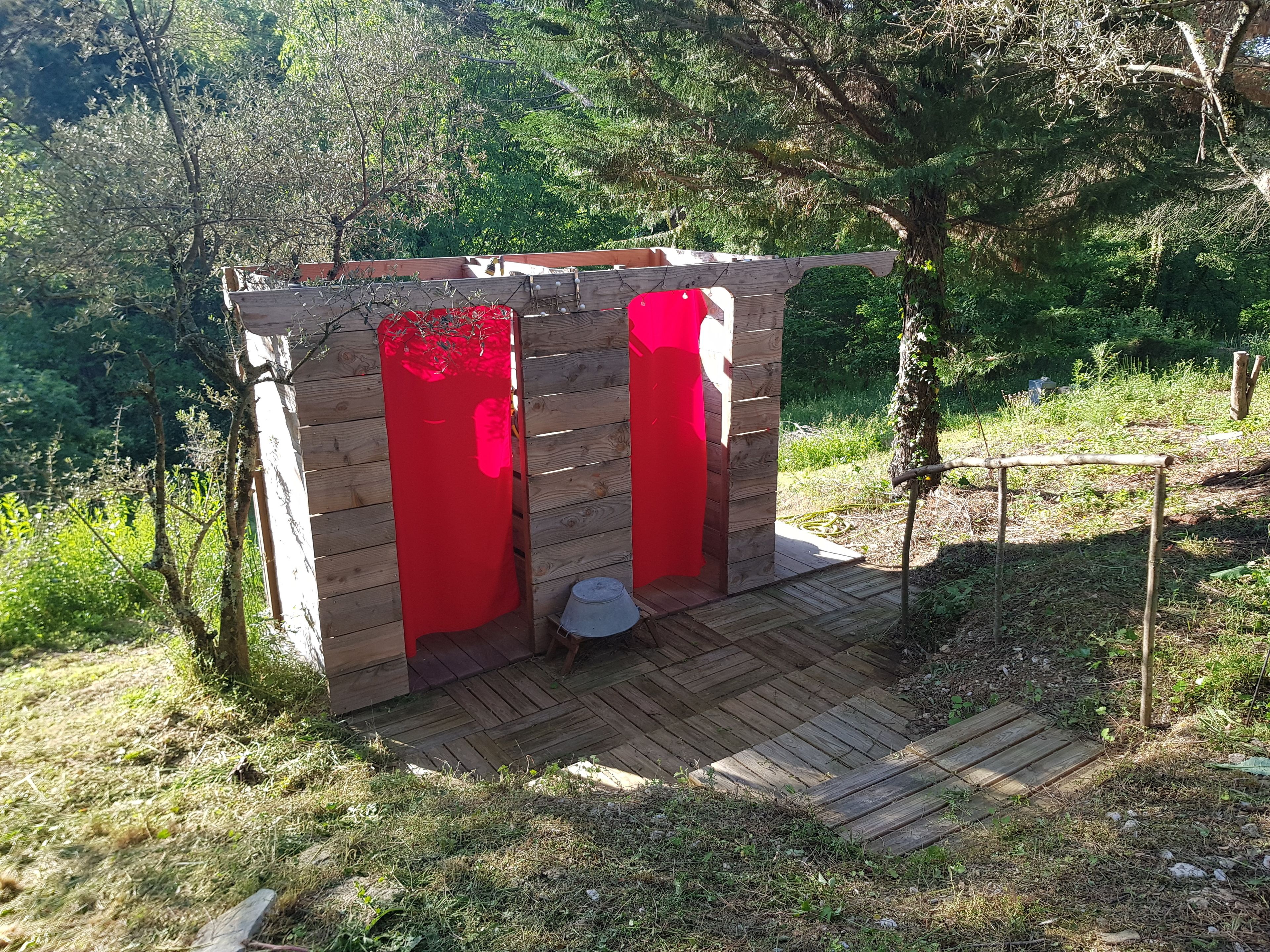 Une structure en bois avec des portes rouges, une petite table et un banc.