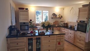 A modern kitchen with wooden cabinets, a central island, and a large window providing natural light. - Mas des Ballats (Saint-Bauzille-de-Putois)