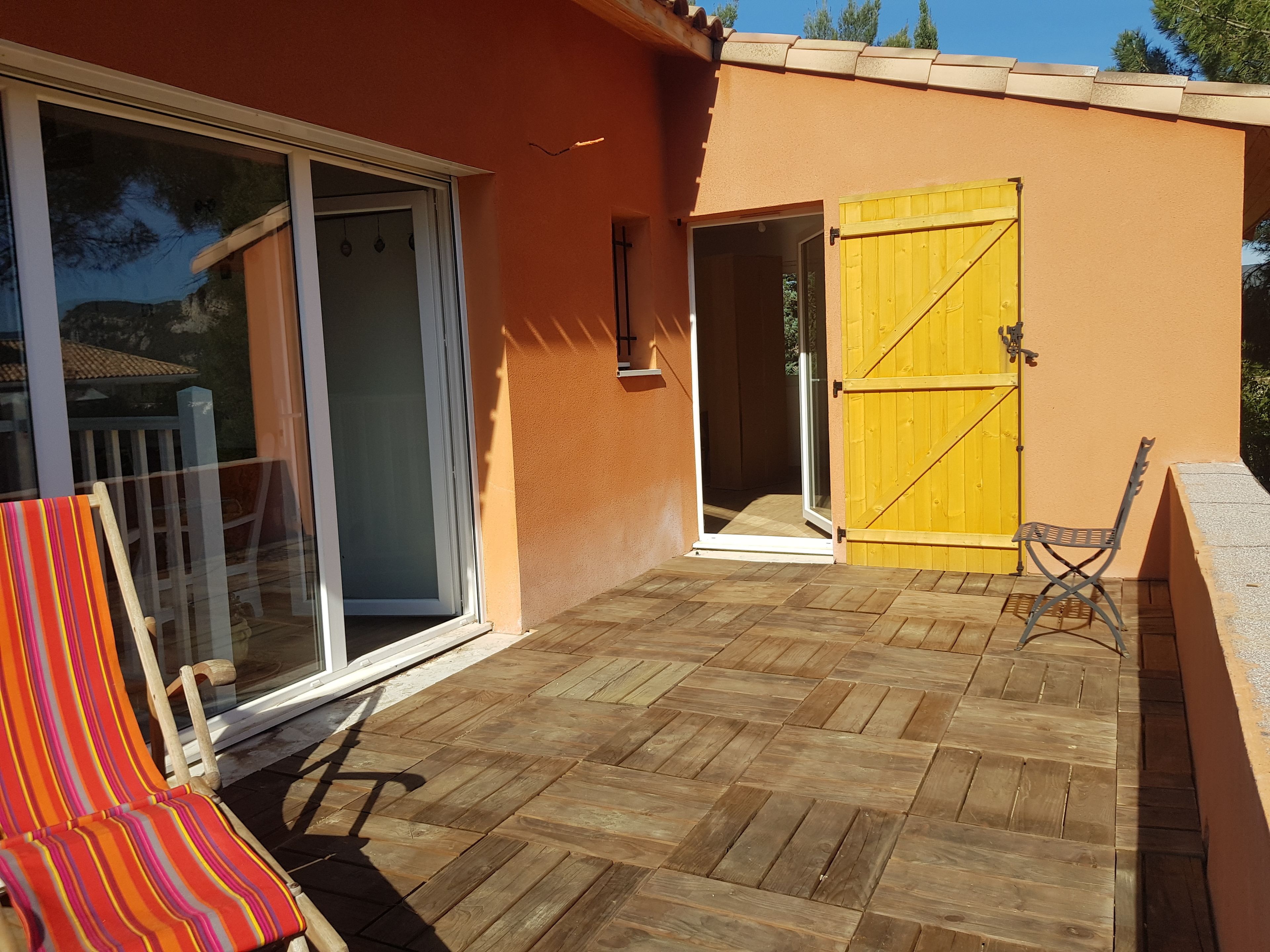 Une terrasse avec un plancher en bois, une porte-fenêtre coulissante, un portail jaune et une chaise à rayures.